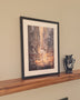 Framed artwork on a wooden shelf against a beige wall